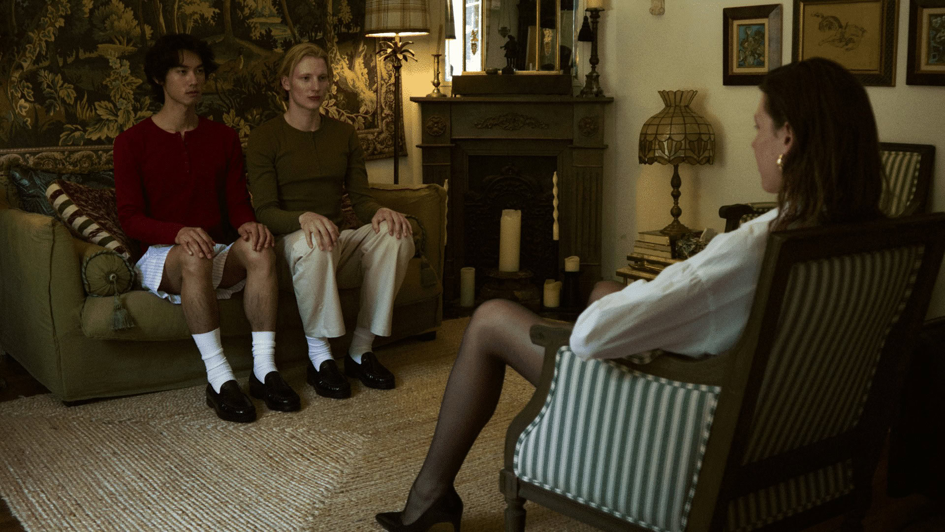 Two women in casual unisex outfits sitting on a sofa, talking to a woman in a white blouse in a cozy.